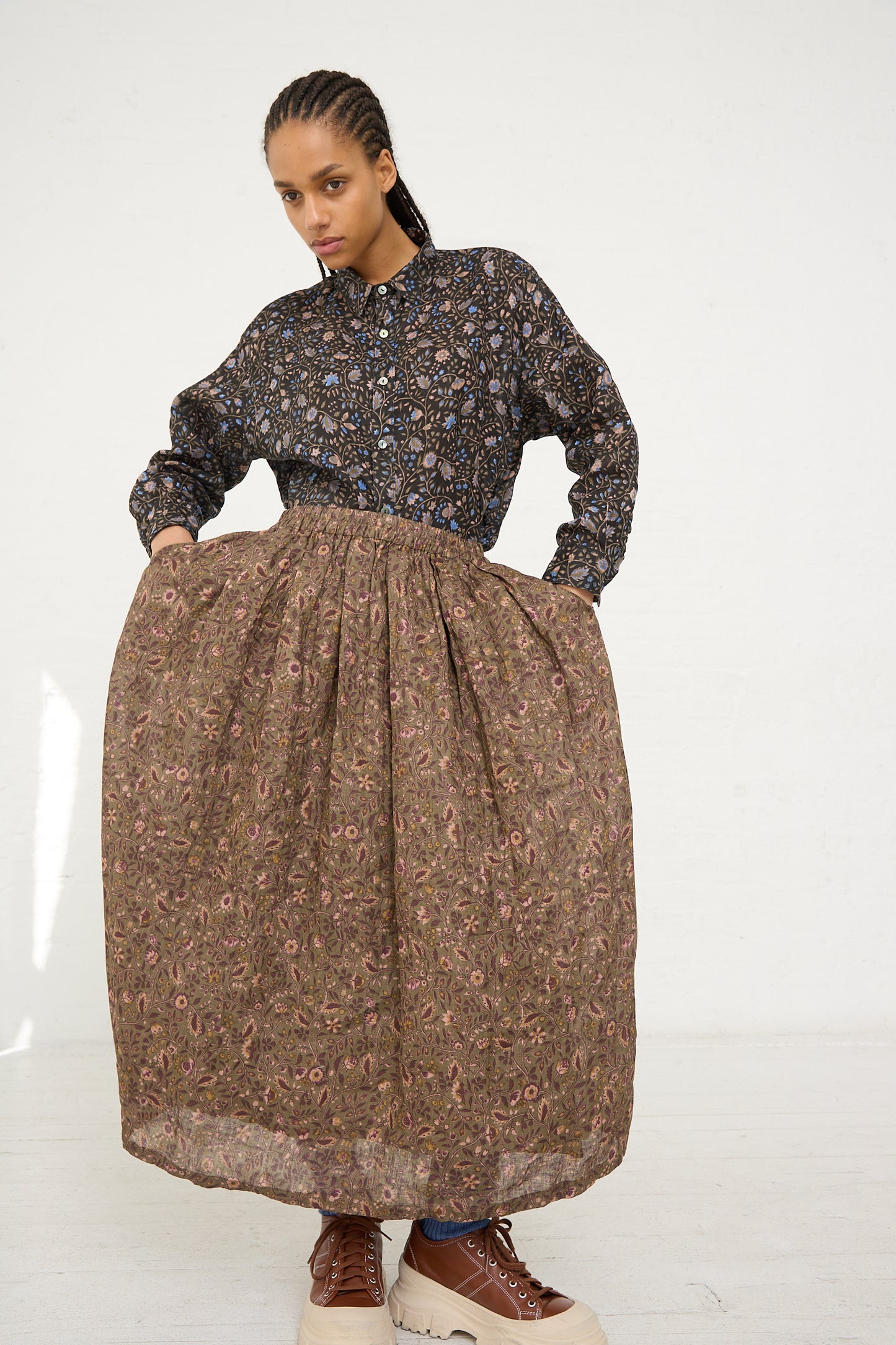 A woman posing in a floral pattern linen dress with puffed sleeves and a voluminous Ichi Antiquités Linen Floral Skirt in Mocha, paired with casual sneakers.