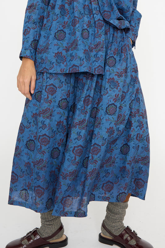 The model is wearing an Ichi Antiquités Linen Floral Skirt in Overdye Blue with gray socks and brown sandals, seen below the waist against a white backdrop.