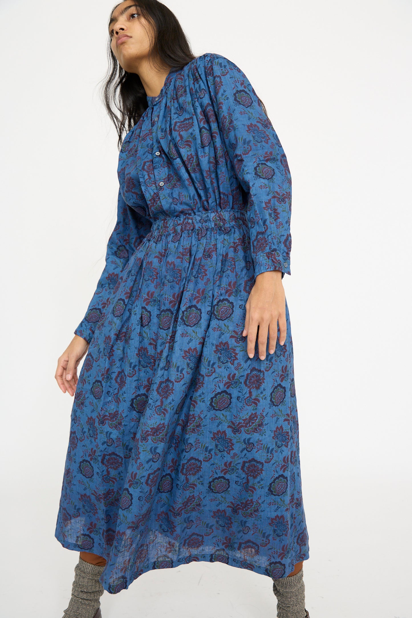 An individual styled in an Ichi Antiquités Linen Floral Skirt in Overdye Blue paired with gray socks is standing against a simple white backdrop.