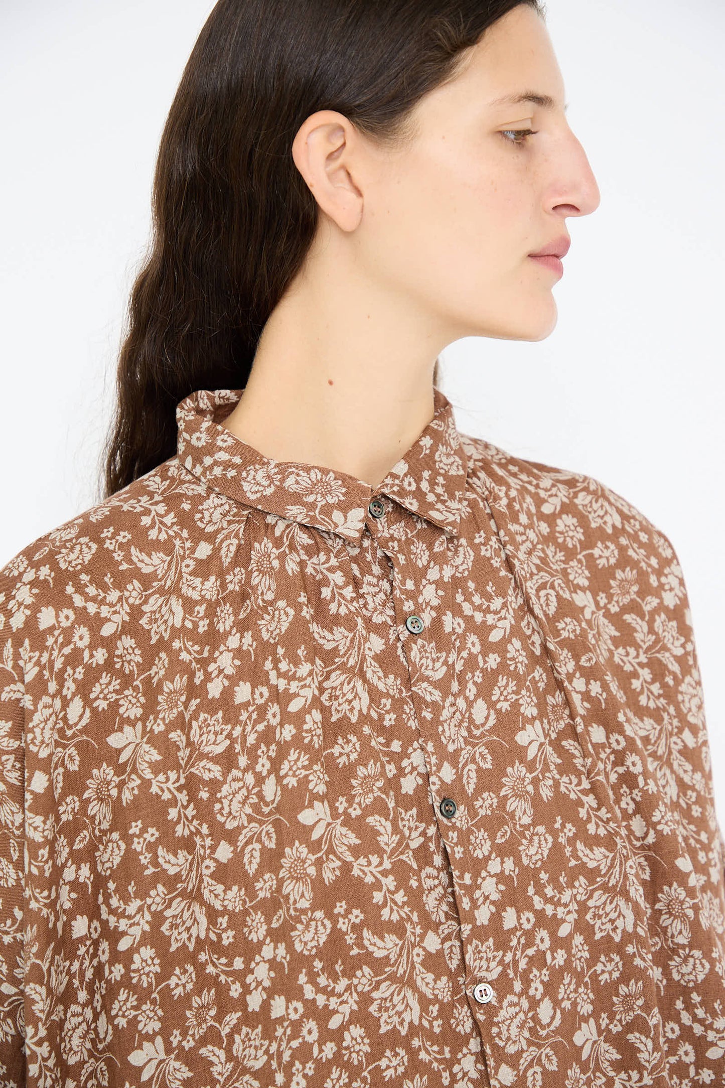 A person with long dark hair is gazing to the side against a plain background, wearing the Linen Flower Print Dress in Brown by Ichi Antiquités.