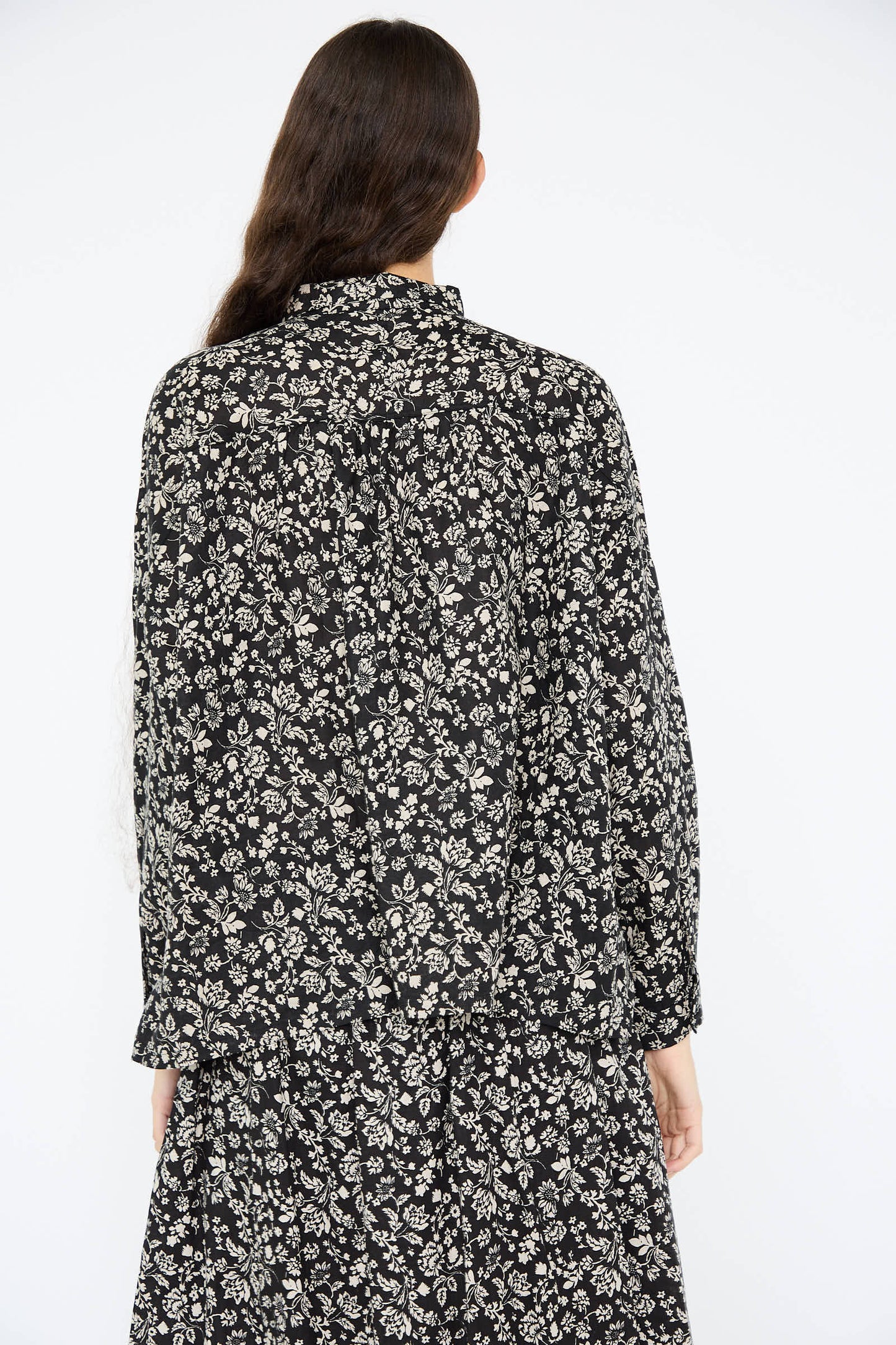 An individual is seen from behind, dressed in an Ichi Antiquités Linen Flower Print Shirt in Black, set against a simple white background and highlighting the intricate black and white floral design.