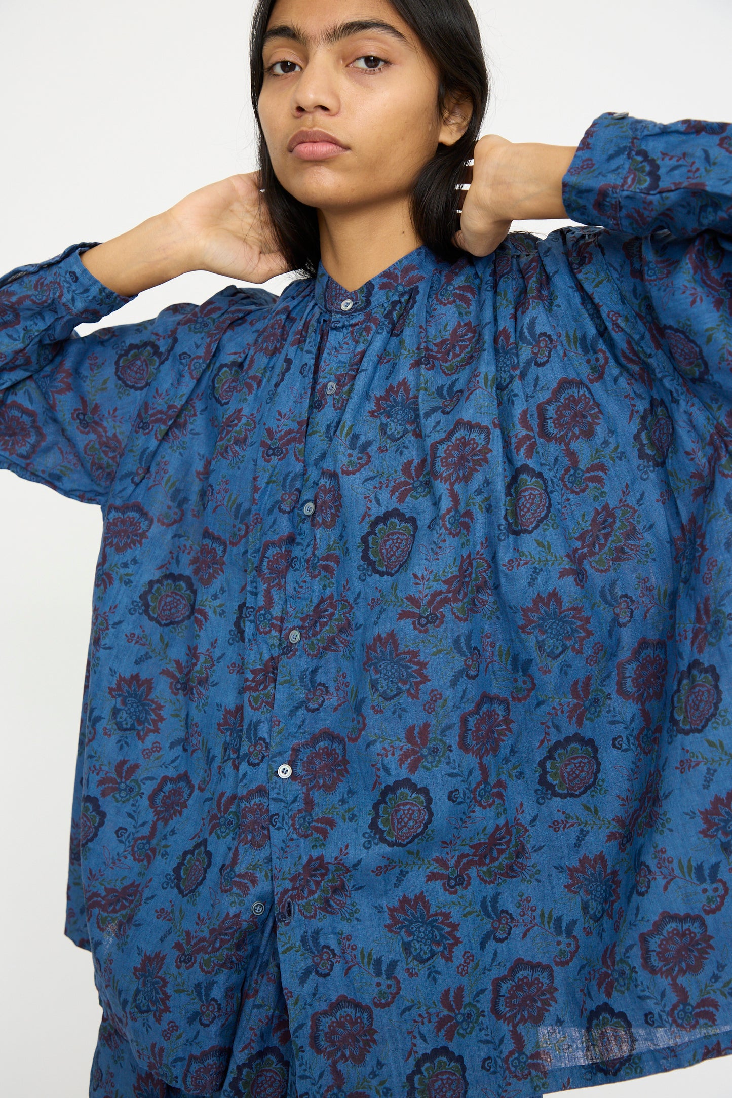 An individual dressed in Ichi Antiquités' Linen Flower Shirt in Overdye Blue adjusts the band collar against a plain backdrop.