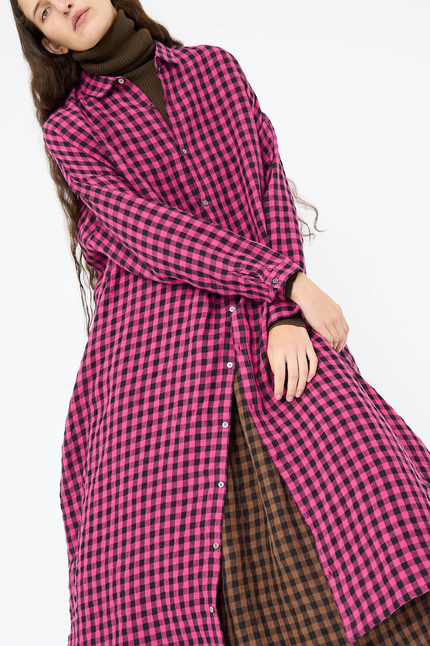 A person in a long-sleeve Linen Gingham Check Dress in Pink by Ichi Antiquités over a brown checkered garment, standing against a plain background.