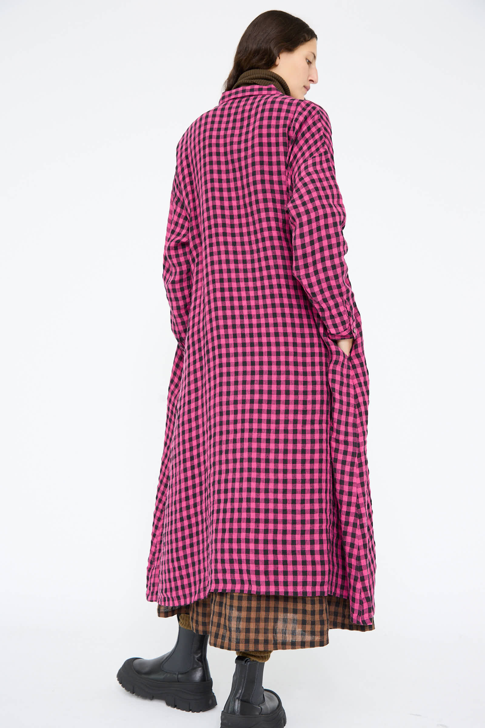 A person in a Linen Gingham Check Dress in Pink by Ichi Antiquités, paired with a brown plaid skirt and black boots, is facing away.