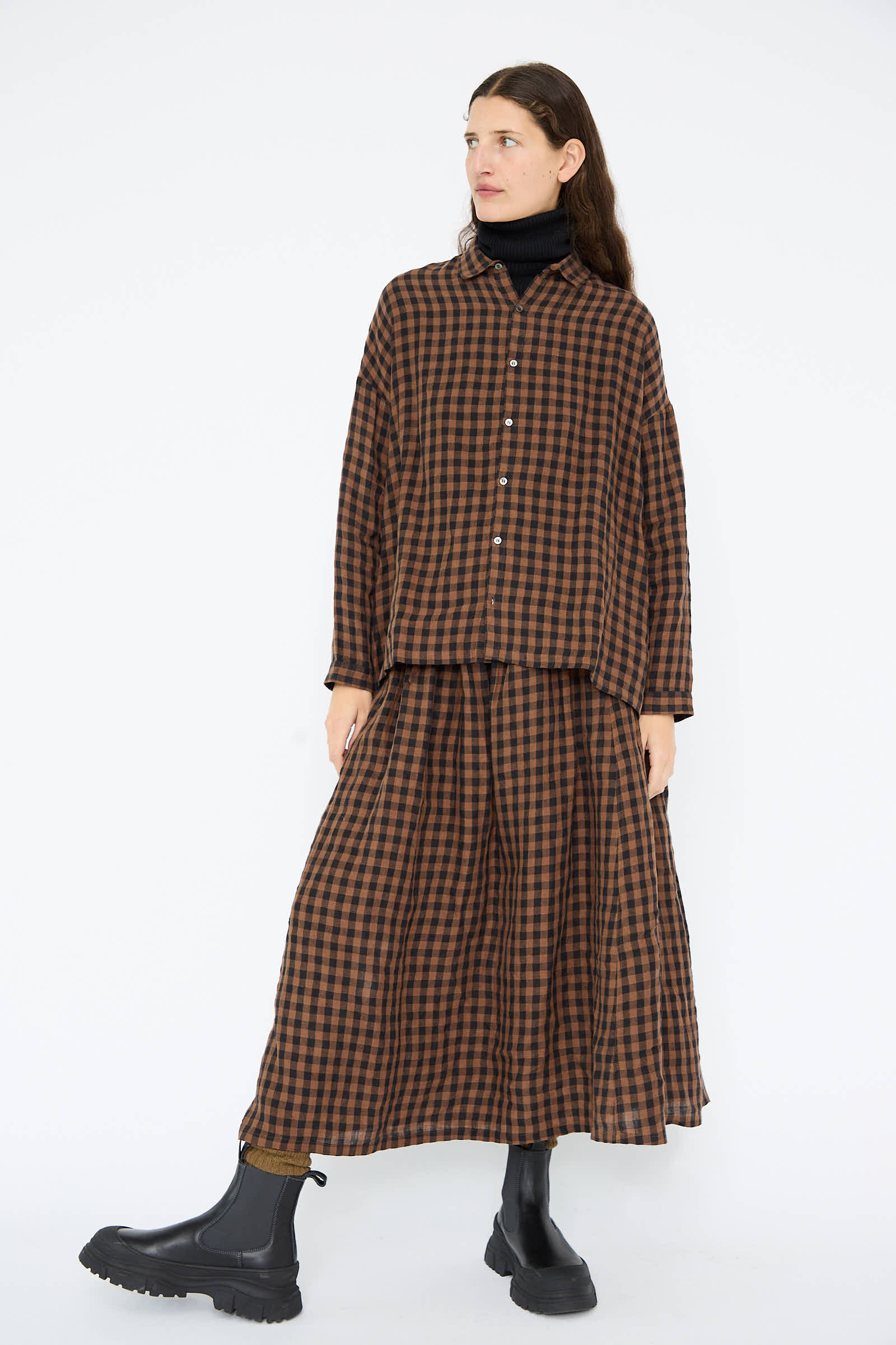 Someone wearing a brown plaid long-sleeve top paired with the Linen Gingham Check Skirt in Brown by Ichi Antiquités and black boots, stands against a white background.