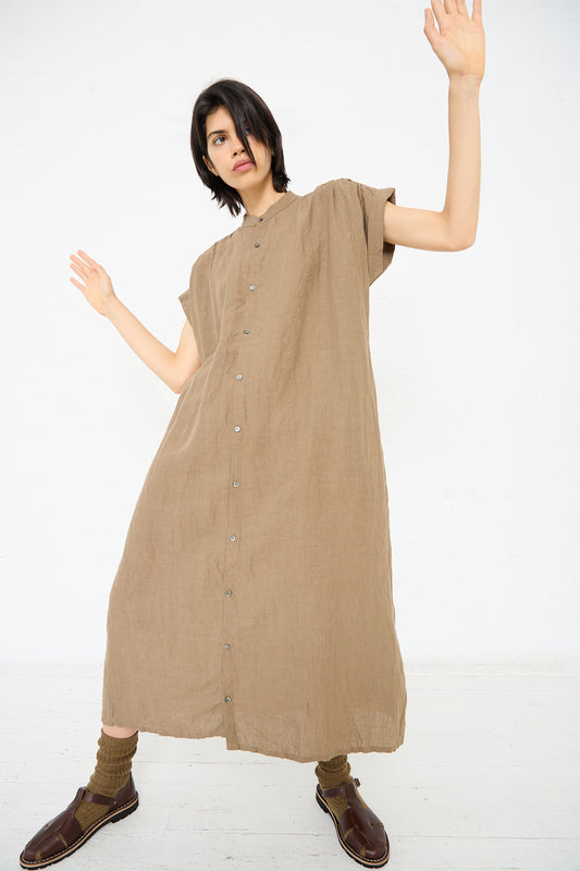 Person wearing a loose-fitting, Ichi Antiquités Linen Natural Washer Dress in Brown with short sleeves, knit socks, and brown shoes, posing with arms raised against a plain white background.