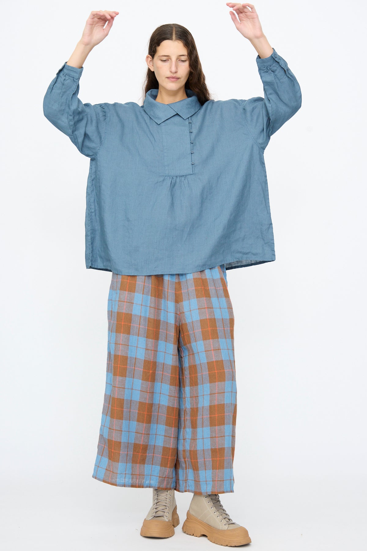 A person wearing an Ichi Antiquités Linen Shirt in Earth Blue, blue and brown plaid wide-leg trousers, and tan lace-up boots with raised soles.