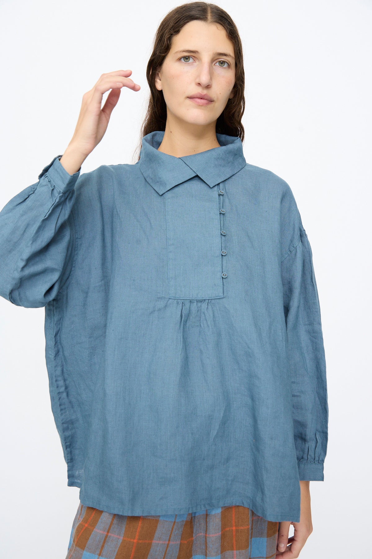 A person wears an Ichi Antiquités Linen Shirt in Earth Blue, a relaxed-fit, long-sleeve shirt with a partial button placket and a collared neckline.