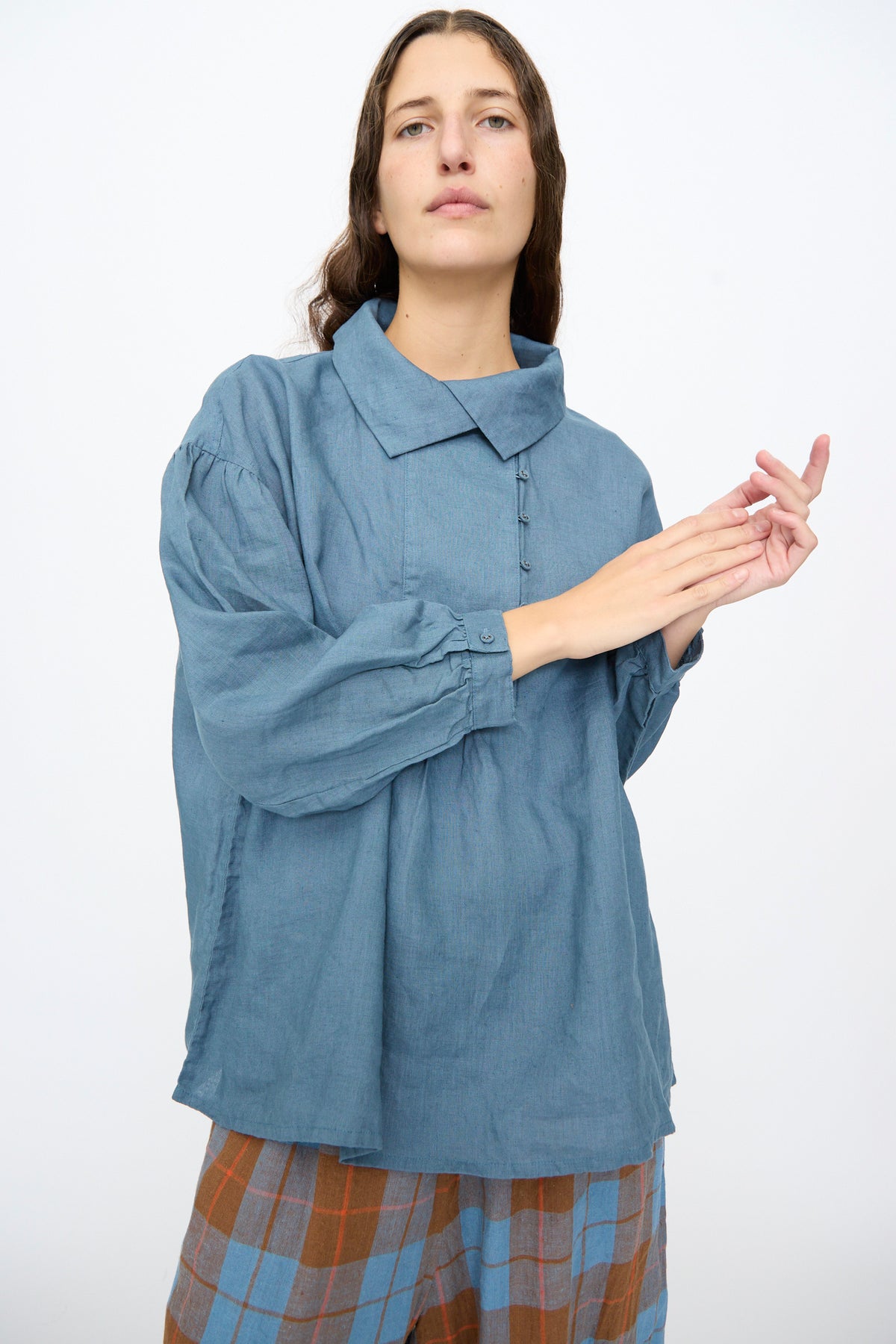 A person wearing an Ichi Antiquités Linen Shirt in Earth Blue with a relaxed fit, collar, and gathered sleeves, paired with brown and blue plaid pants.