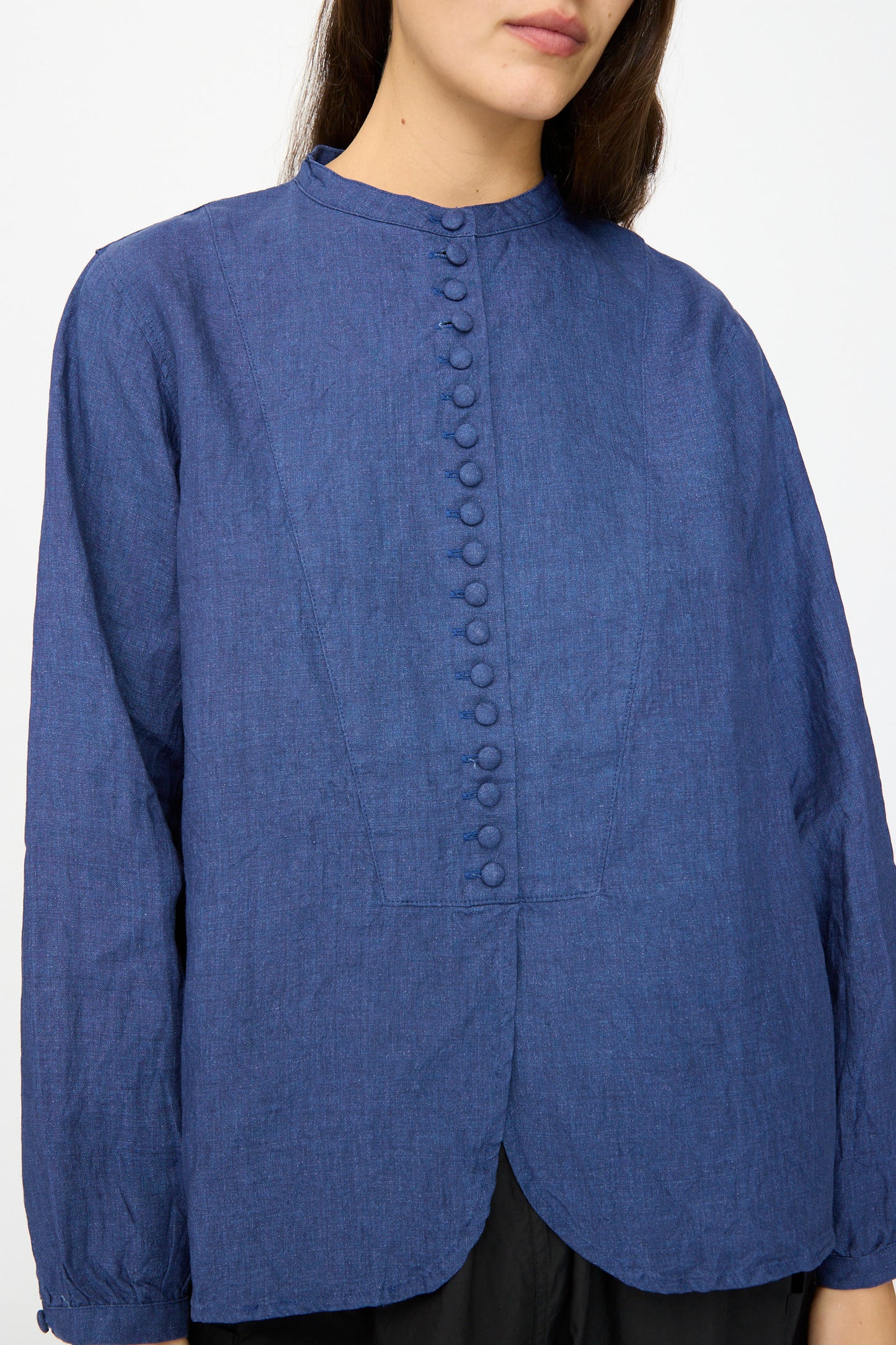 A woman wears the Ichi Antiquités Linen Shirt in Indigo, featuring long sleeves, a band collar, and a scalloped hem, made in Japan.