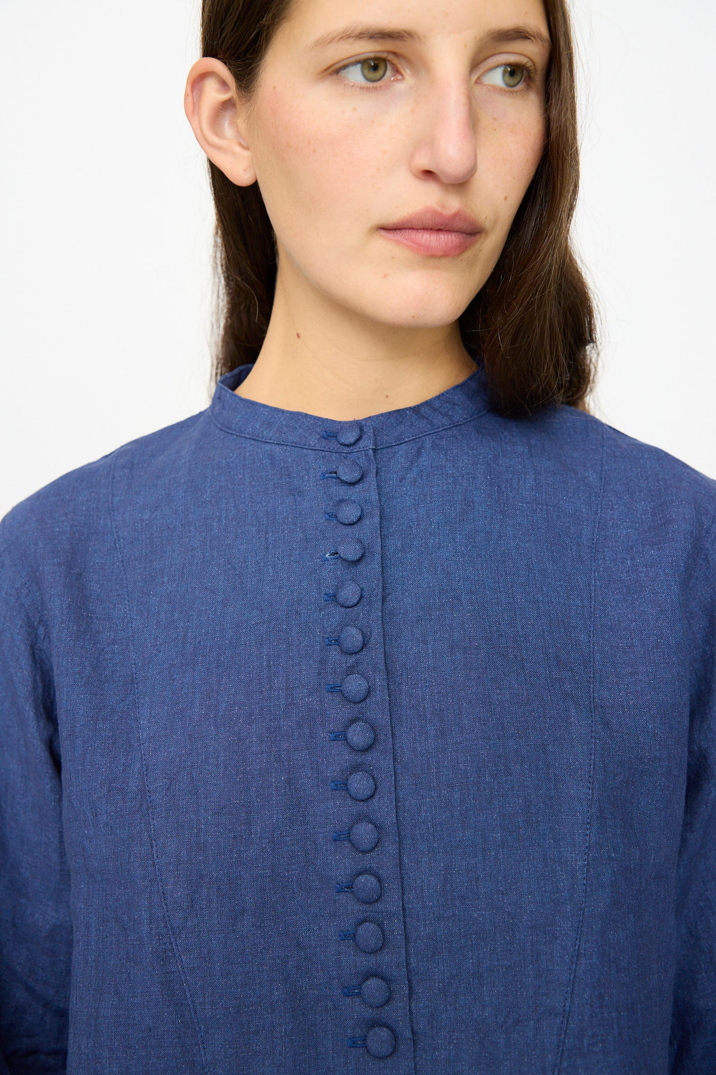 A woman shown from the shoulders up wears the Ichi Antiquités Linen Shirt in Indigo, featuring a band collar and fabric-covered buttons down the front.