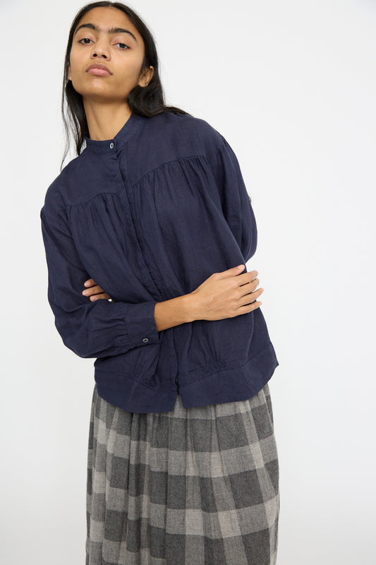 A person wearing the Ichi Antiquités Linen Shirt in Navy with a relaxed fit and a gray plaid skirt stands with arms crossed, looking slightly sideways.