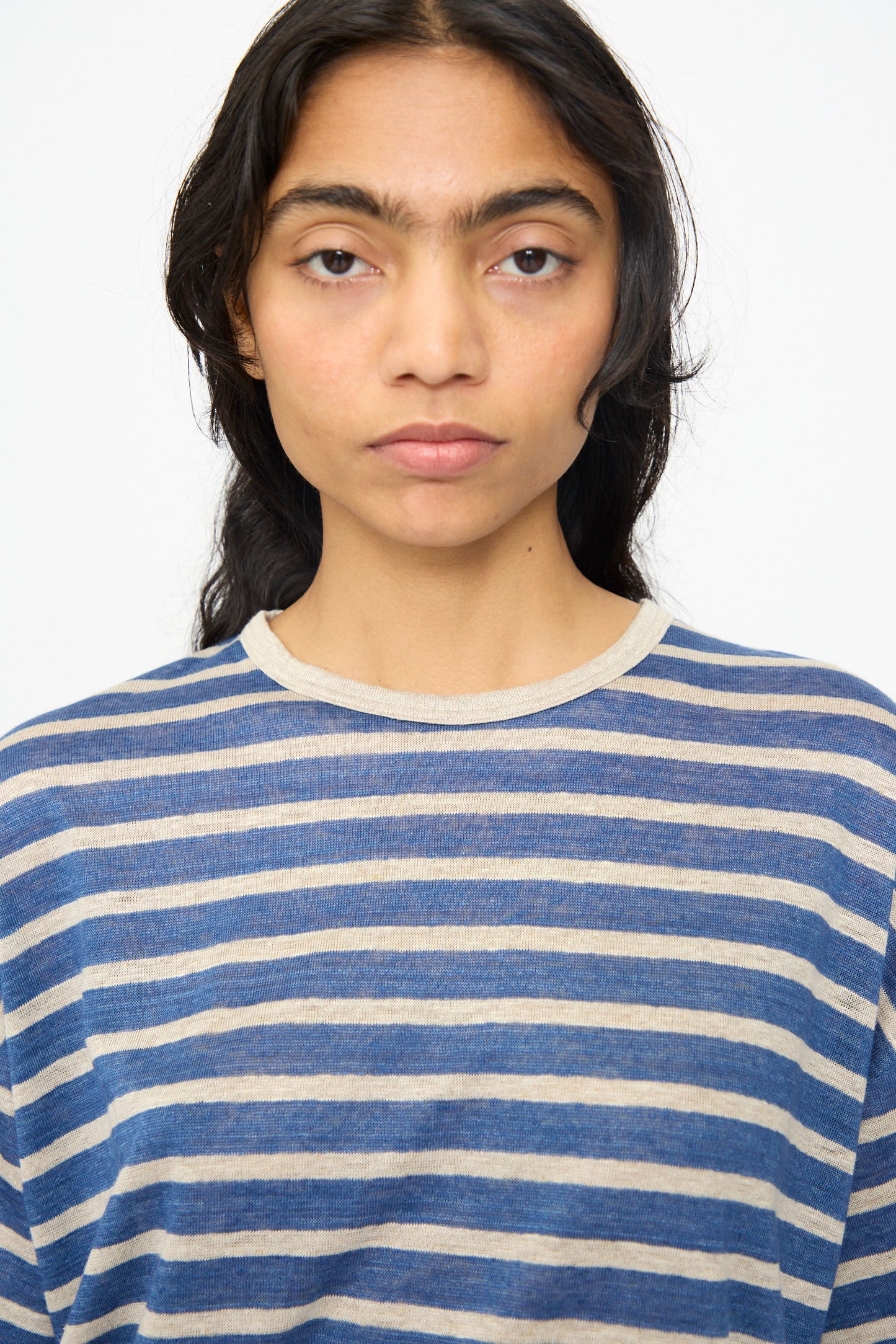 Person with long dark hair wearing the Ichi Antiquités Linen Stripe Pullover in Blue and Natural, boxy fit, looking straight at the camera against a plain white background. Made in Japan.