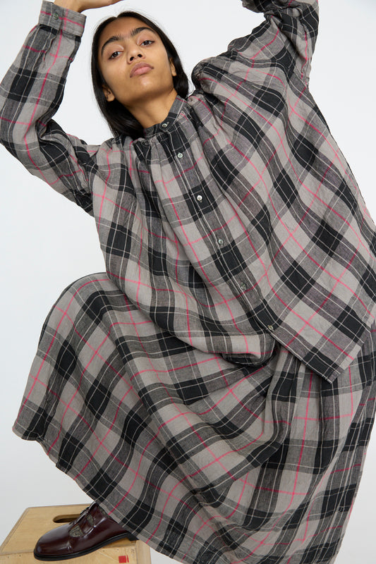 Wearing a relaxed fit, Linen Tartan Shirt in Gray with a band collar from Ichi Antiquités, a person poses with arms raised on a wooden platform.