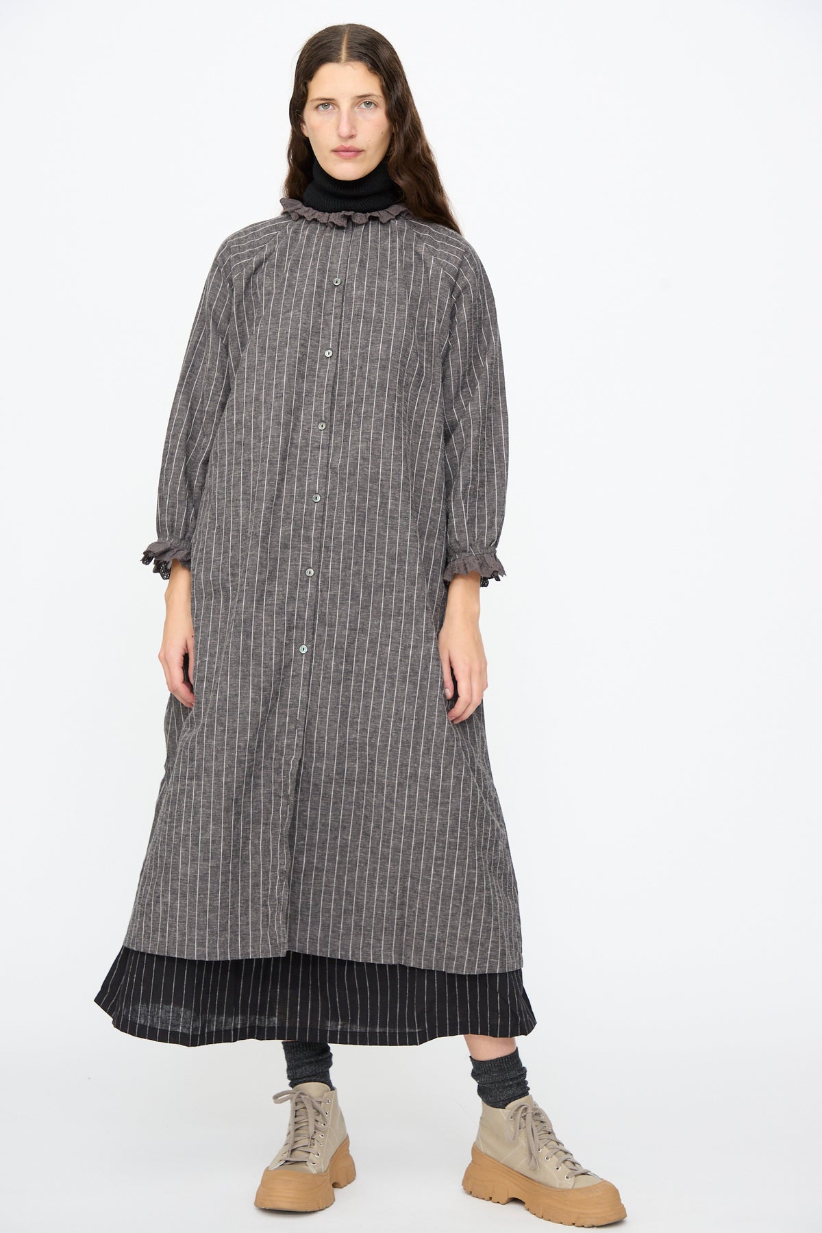 Ichi Antiquités Pinstripe Dress in Charcoal, a midi-length linen design with a lace ruffle collar and button-down front, worn over a black skirt and beige lace-up boots.
