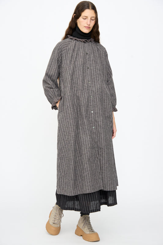 A person wears an Ichi Antiquités Pinstripe Dress in Charcoal over a black turtleneck and skirt, finished with beige lace-up boots.