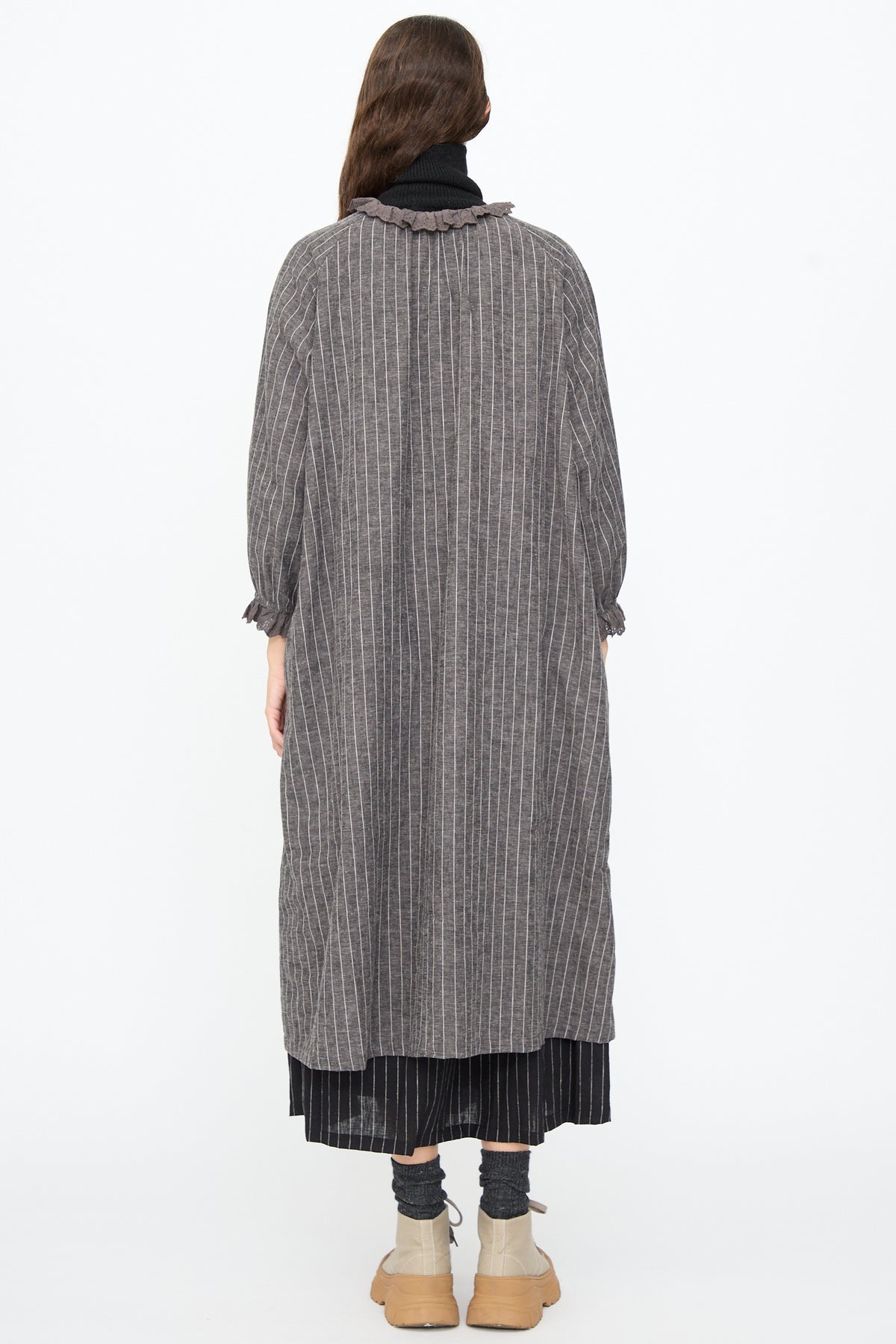 A person viewed from behind wearing an Ichi Antiquités Pinstripe Dress in Charcoal, styled with a lace ruffle collar and cuffs, grey socks, and tan platform boots.