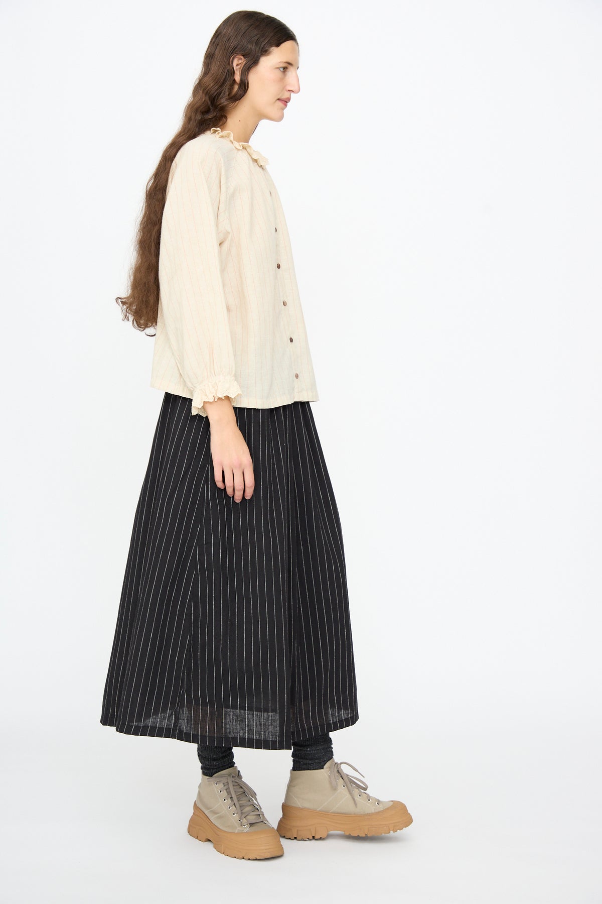 A person wearing an Ichi Antiquités Pinstripe Shirt in Natural with a lace ruffle collar and cuffs, a black pinstripe maxi skirt, and beige platform boots.