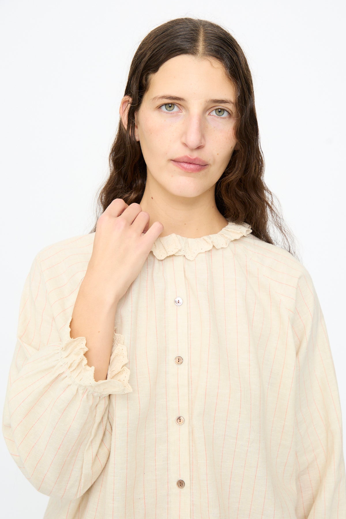 A person wears an Ichi Antiquités Pinstripe Shirt in Natural, a relaxed-fit beige shirt featuring thin vertical red stripes and a ruffled collar.