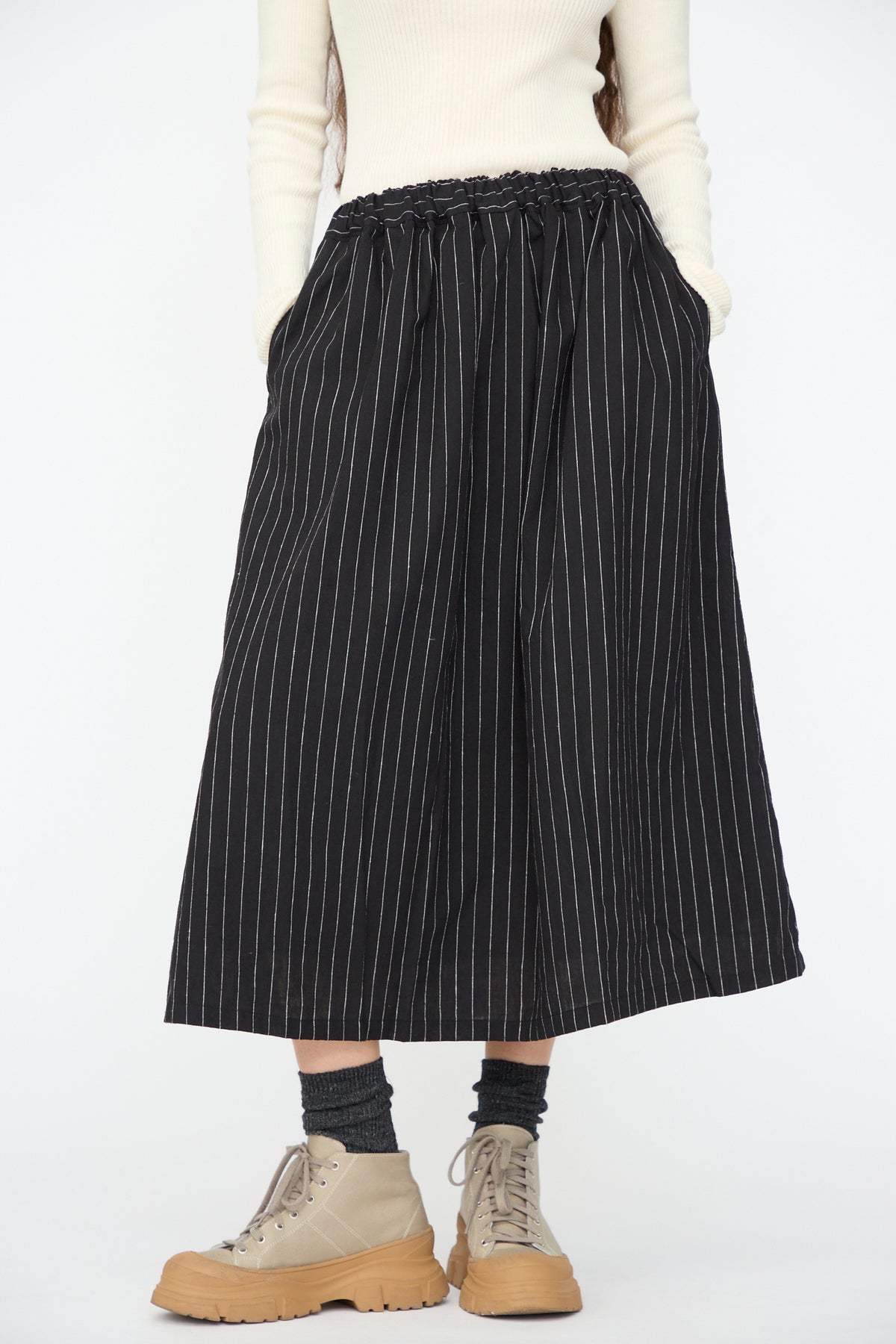 A person wearing an Ichi Antiquités Pinstripe Skirt in Black, an off-white ribbed long-sleeve top, charcoal socks, and beige platform sneakers.