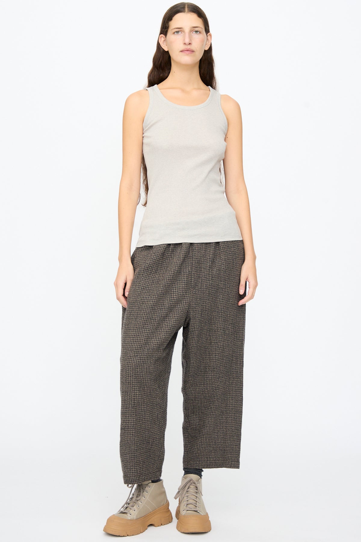 A person wearing a gray Ichi Antiquités Rib Tank Top, brown patterned loose-fitting trousers, and beige high-top sneakers.