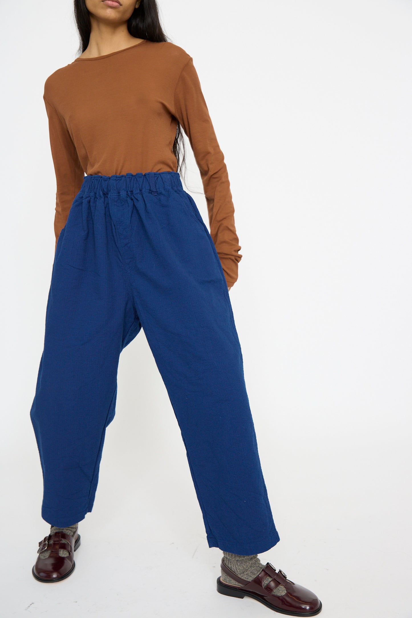 A person in a long-sleeved brown top and Ichi Antiquités' Sashiko Pants in Indigo, featuring a wide-leg relaxed fit, poses against a plain white background with brown shoes.