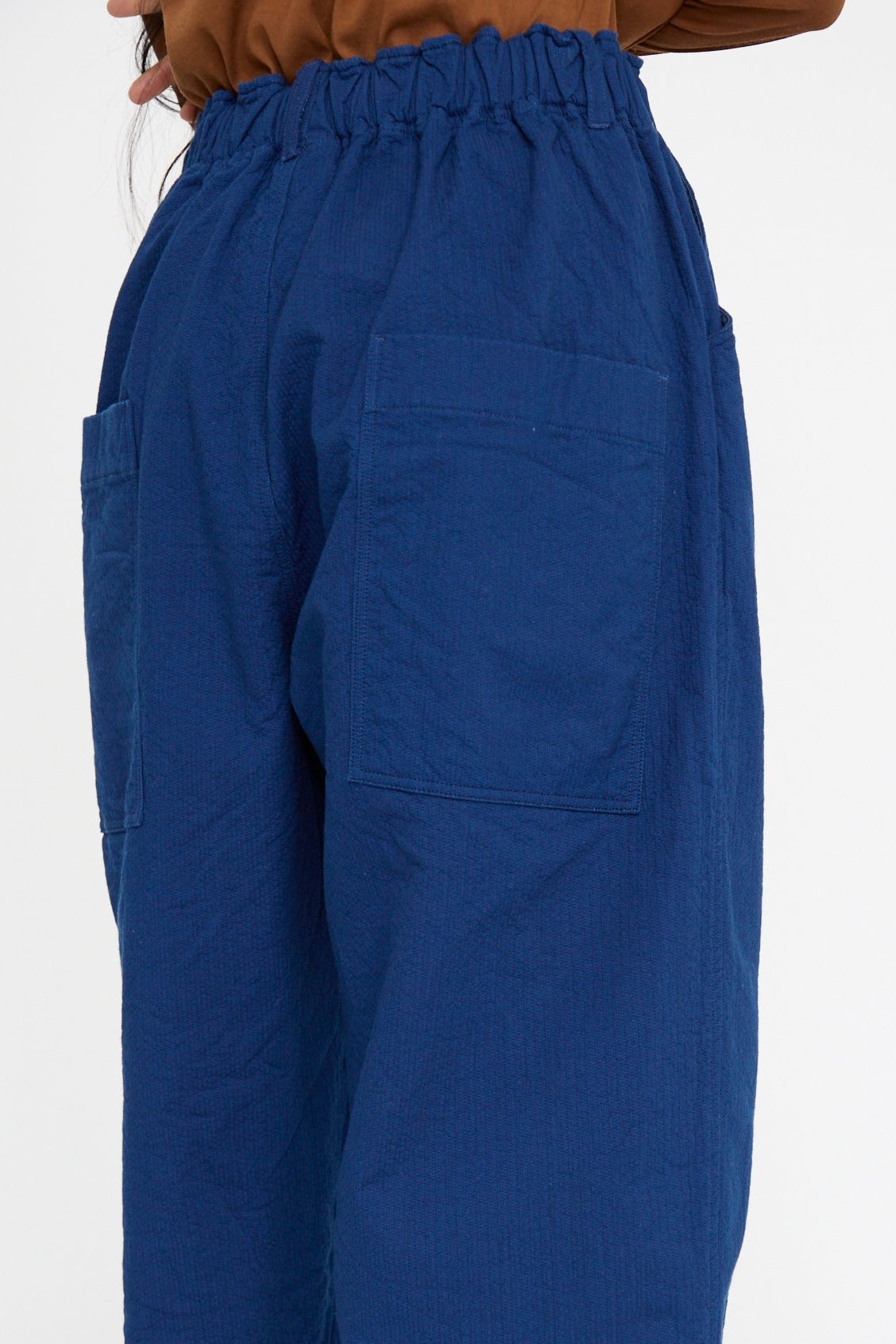 A close up of the waistline of a person wearing Ichi Antiquités' Sashiko Pants in Indigo, crafted from relaxed fit cotton with wide legs, large back pockets, and an elastic waistband.