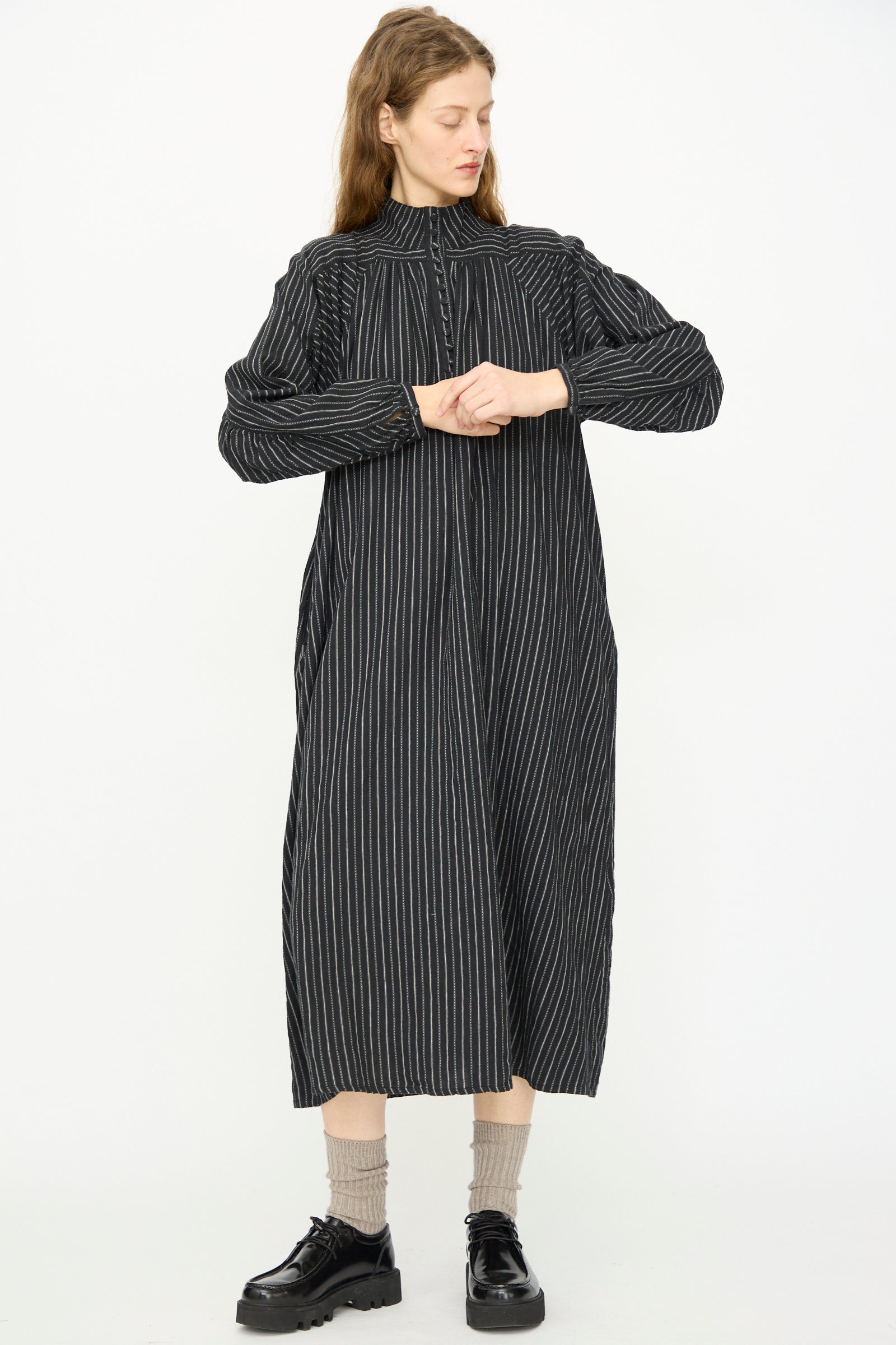 A person faces forward in the Shirring Brushed Stripe Dress in Black by Ichi Antiquités, featuring thin white stripes, tan socks, and black shoes against a plain white background.