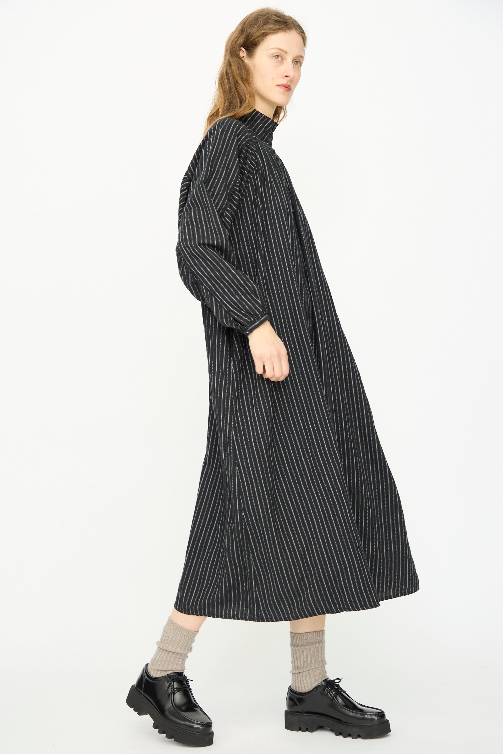 A person wears the Ichi Antiquités Shirring Brushed Stripe Dress in Black with beige socks and black platform shoes, standing against a plain white background.