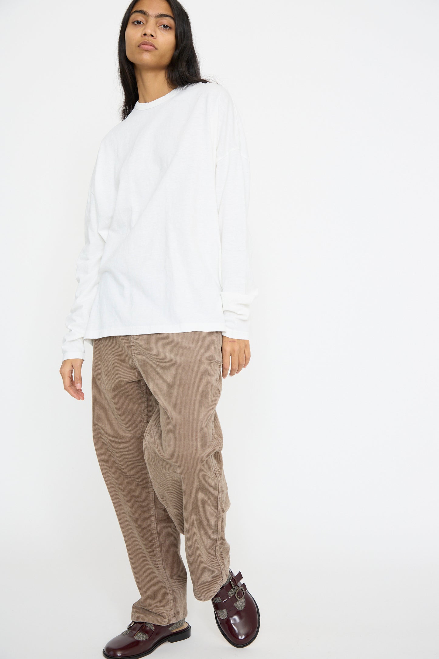 A person wearing a white long-sleeve shirt, Ichi Antiquités Stretch Call Corduroy Pants in Mocha, and dark shoes stands against a white background.