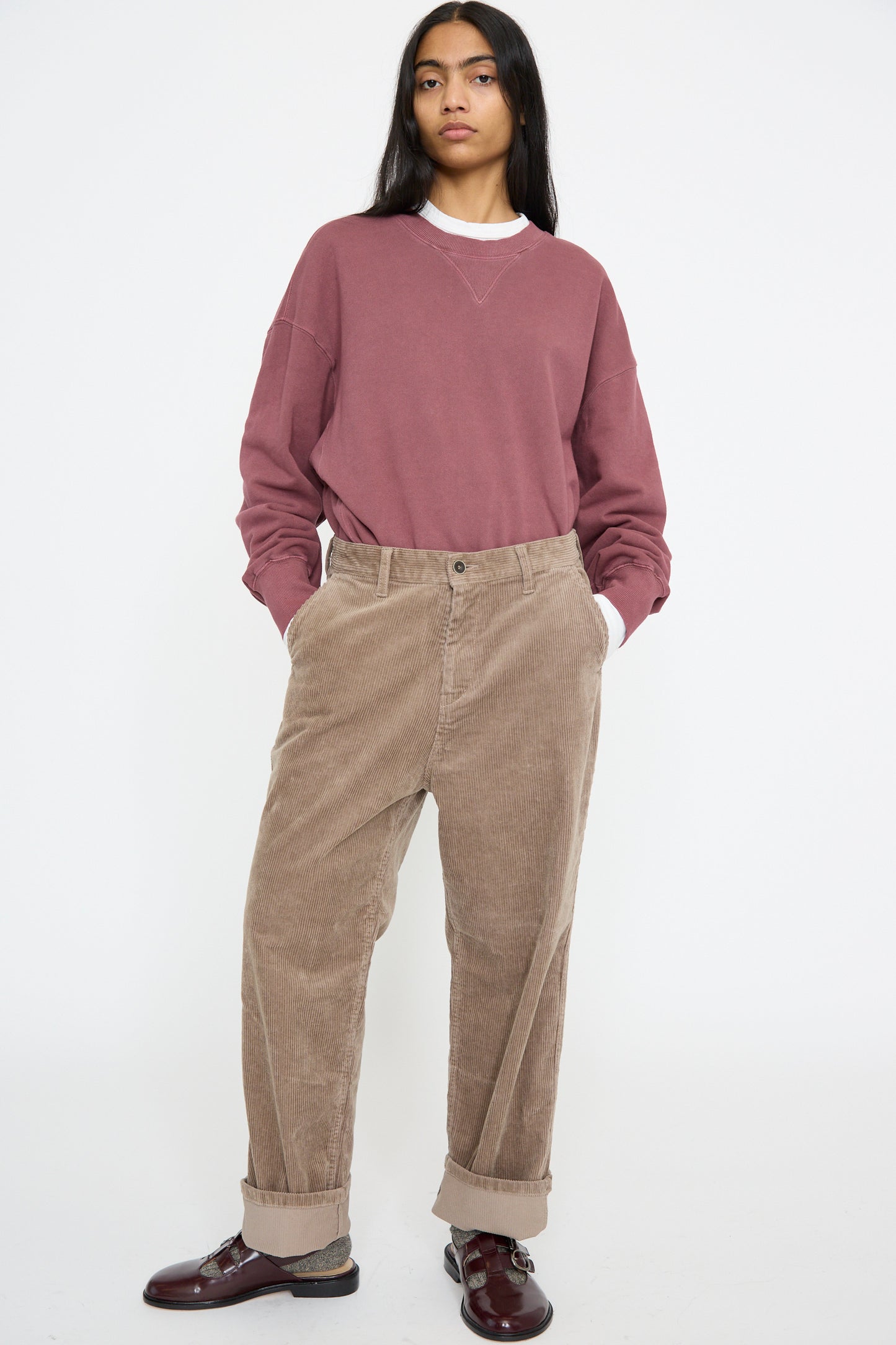 A person in a maroon sweatshirt and Ichi Antiquités Stretch Call Corduroy Pants in Mocha with hands in pockets, standing against a plain background.