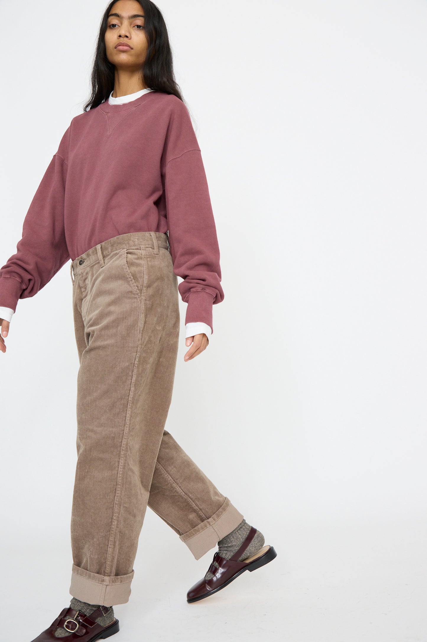 A person wearing Ichi Antiquités' mauve sweatshirt and Stretch Call Corduroy Pants in Mocha is walking against a plain white background, with dark brown shoes.