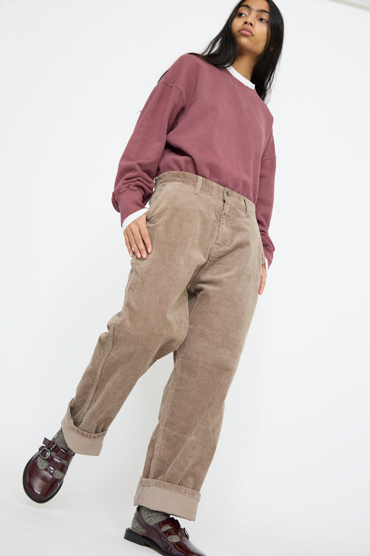 A person stands casually wearing a maroon sweatshirt, Ichi Antiquités Stretch Call Corduroy Pants in Mocha, burgundy shoes, and gray socks against a plain background.