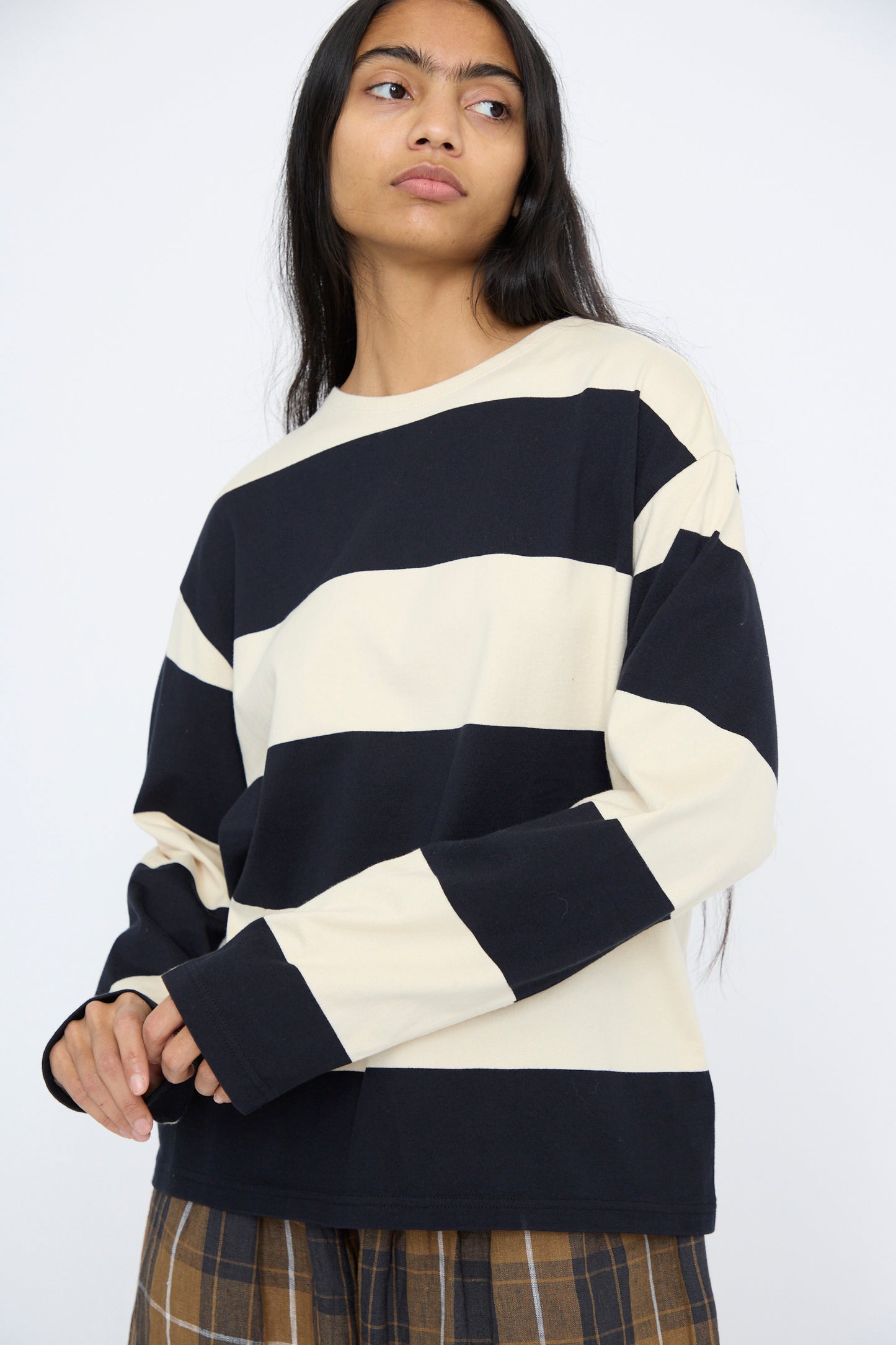 A person wearing the Striped Crewneck in Beige and Black by Ichi Antiquités, featuring a relaxed fit and paired with plaid pants, stands against a plain white background.