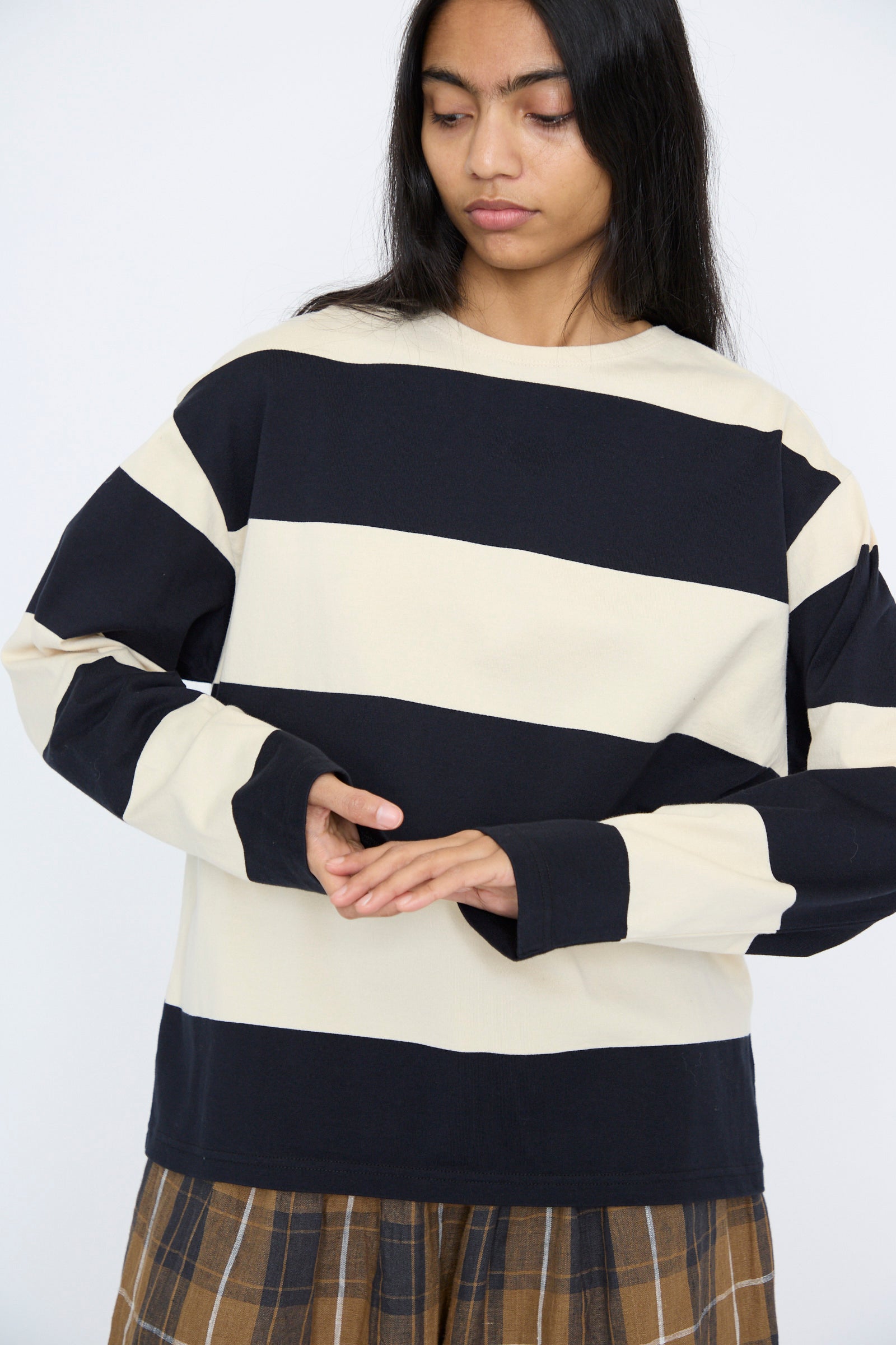 Person in a Striped Crewneck in Beige and Black by Ichi Antiquités, paired with a brown plaid skirt, featuring long dark hair and standing against a plain background.