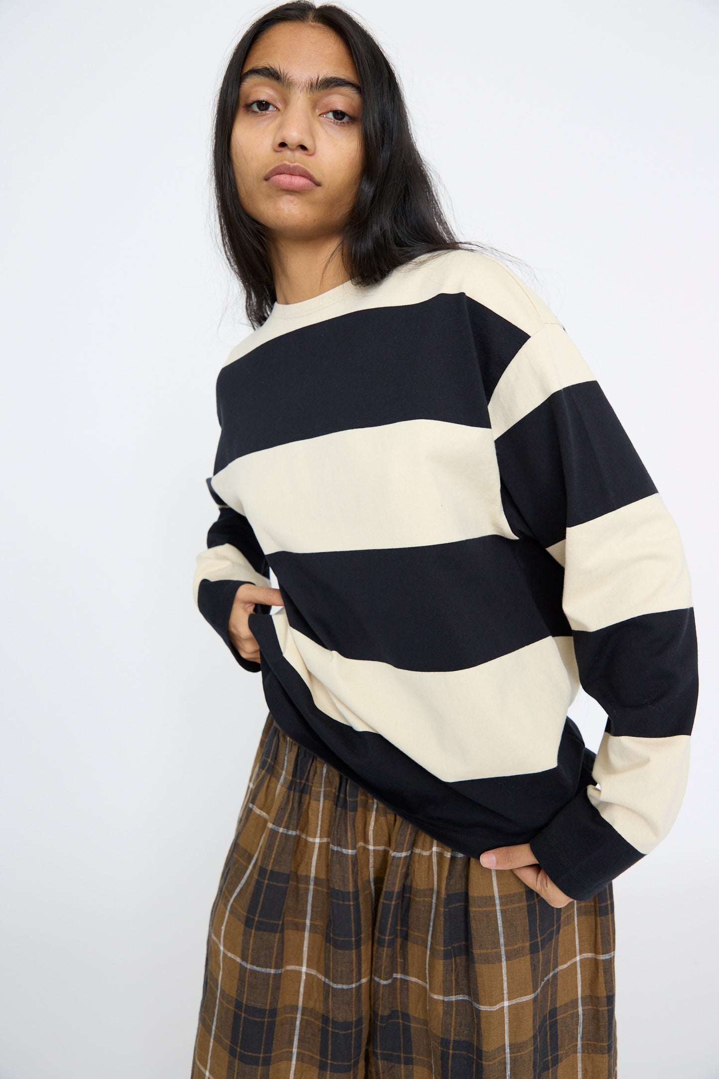 A relaxed fit in an Ichi Antiquités Striped Crewneck in Beige and Black, paired with brown plaid pants, stands against a plain background.