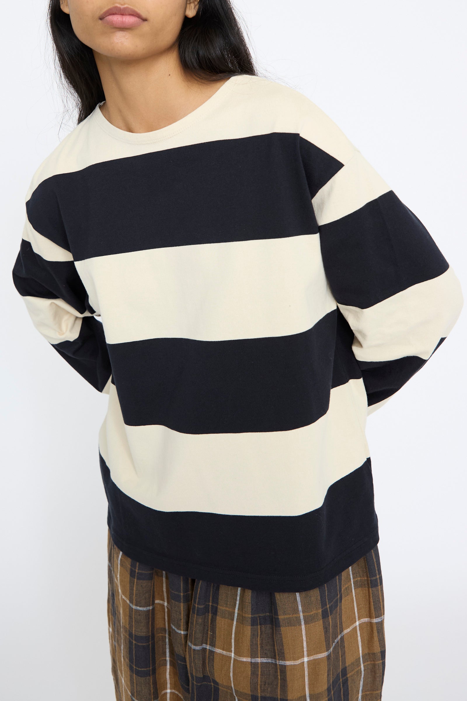 A person is wearing the Ichi Antiquités Striped Crewneck in Beige and Black paired with a plaid skirt, standing against a plain background.