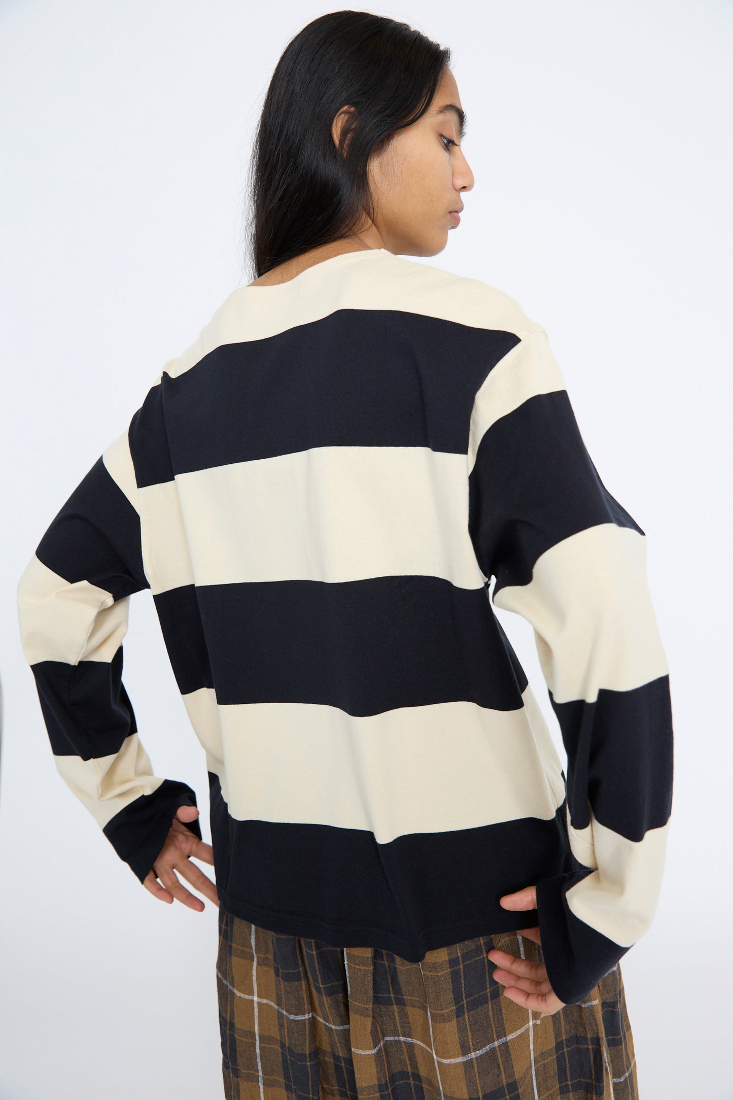 A person wears the Ichi Antiquités Striped Crewneck in Beige and Black with plaid pants, standing with their back to the camera against a plain background.