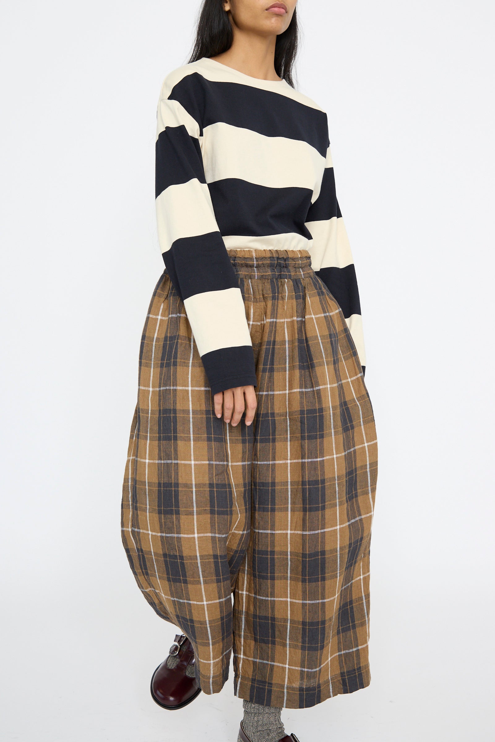 A person is wearing the Striped Crewneck in Beige and Black by Ichi Antiquités, paired with brown plaid wide-leg pants against a plain background.