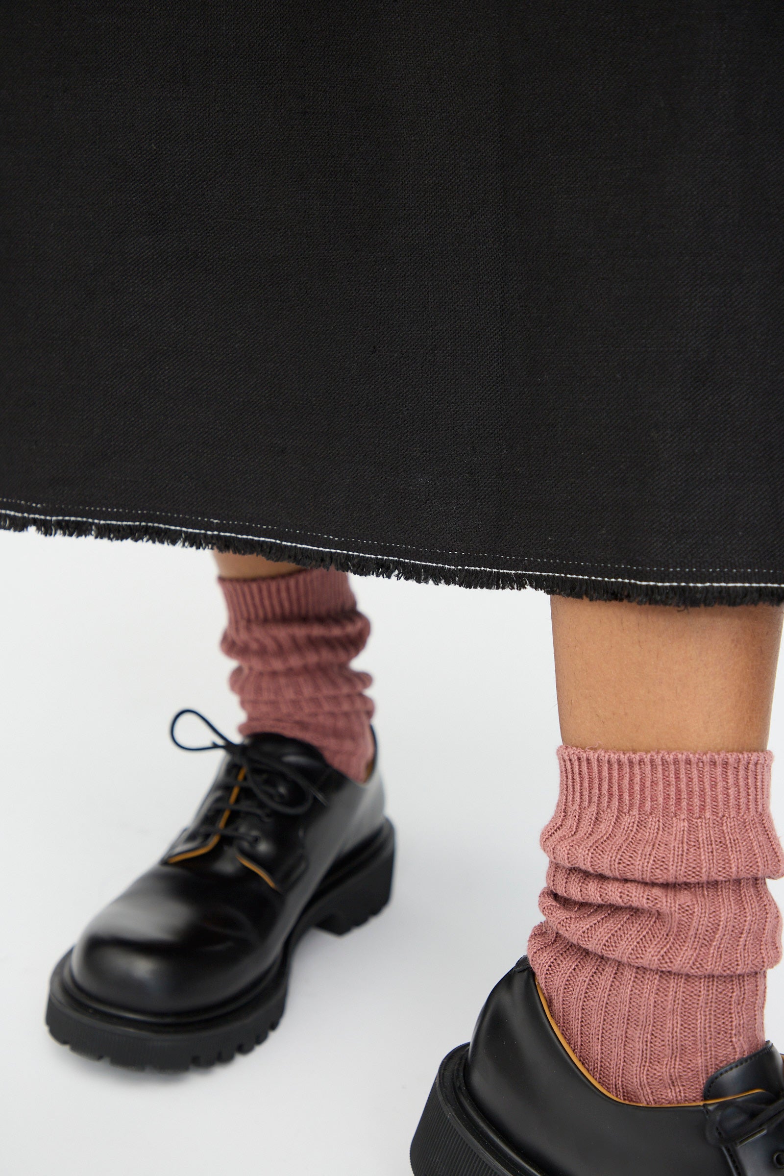 A person wears the Ichi Antiquités Twill Weave Linen Dress in Black with pink ribbed socks and black lace-up shoes, standing on a white background.