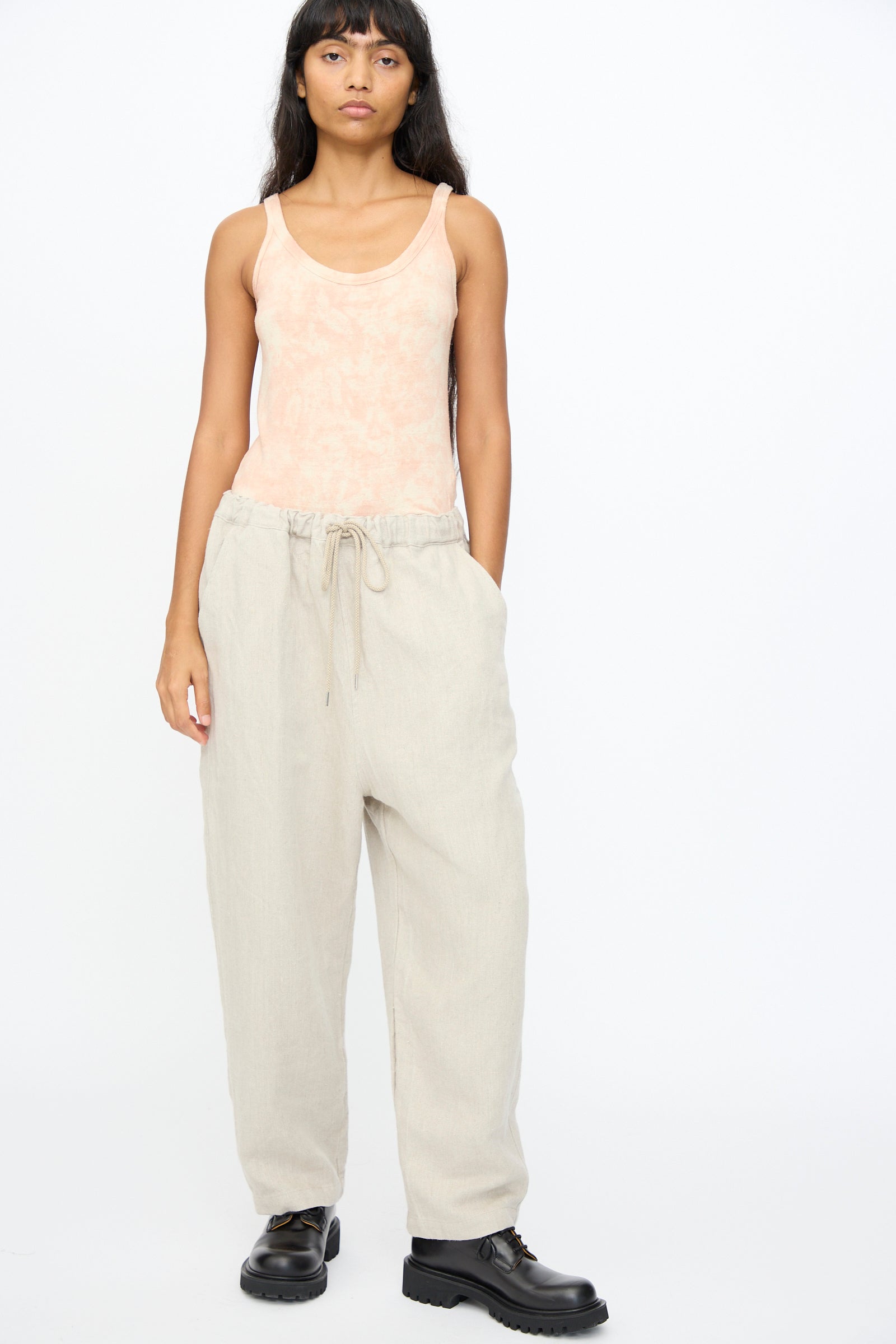 A person stands facing forward wearing a peach tank top, black shoes, and Ichi Antiquités Twill Weave Linen Pant in Natural against a plain white background.