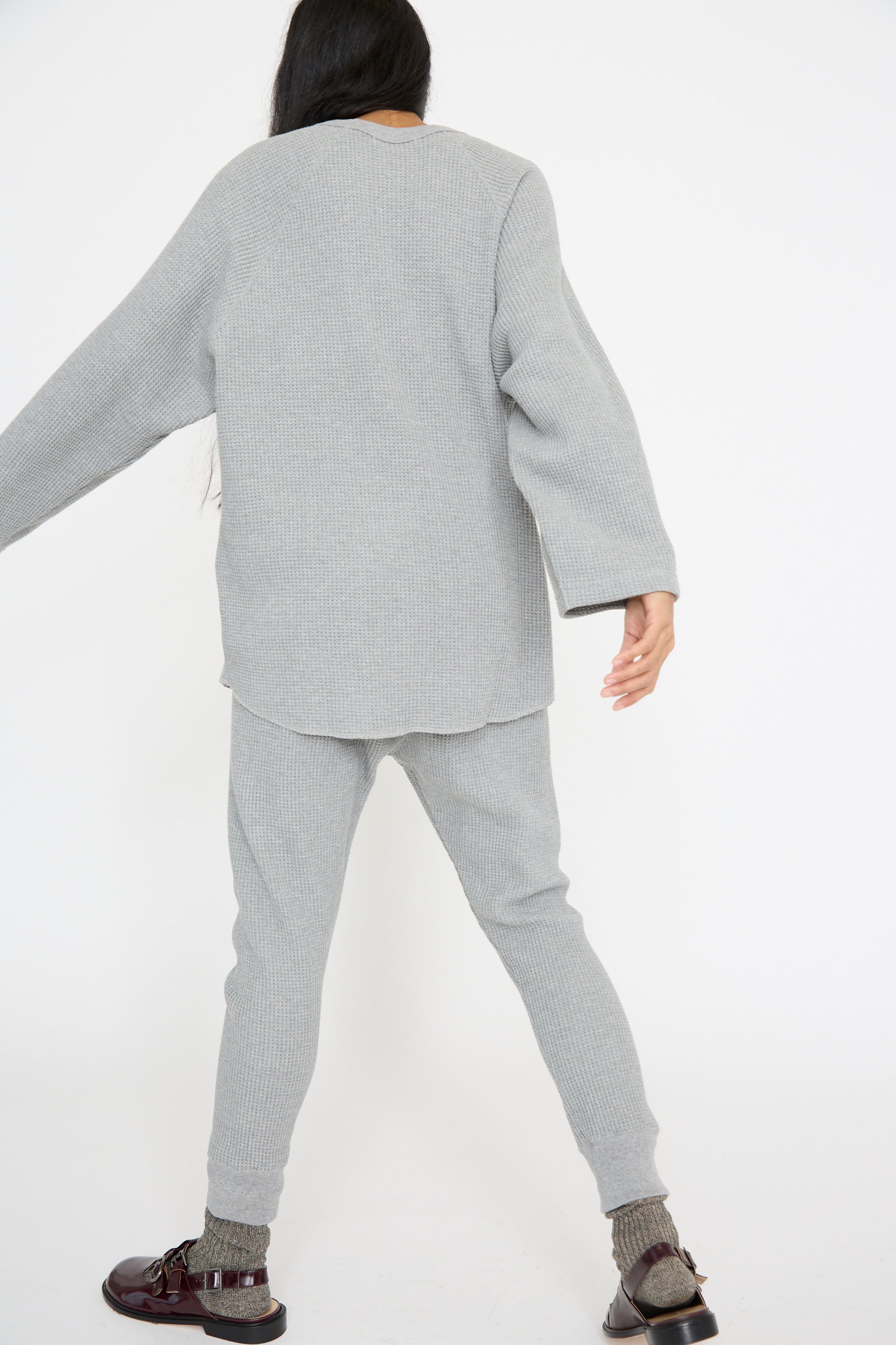 A person wearing an Ichi Antiquités slim fit gray knit sweater and Waffle Knit Pants in Gray, paired with brown shoes, faces away from the camera on a plain white background.