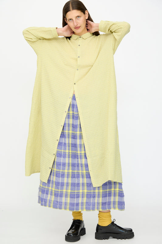 A person wearing the Ichi Antiquités Wool Cotton Gingham Dress in Yellow and Gray stands against a plain white background, styled with yellow socks, black shoes, and a purple and yellow plaid skirt.