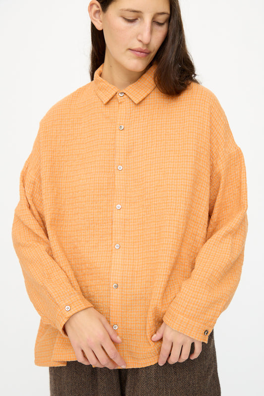 A person wears the Ichi Antiquités Wool Cotton Gingham Shirt in Orange and Mocha, featuring an oversized fit and subtle checkered pattern, standing against a plain light background.