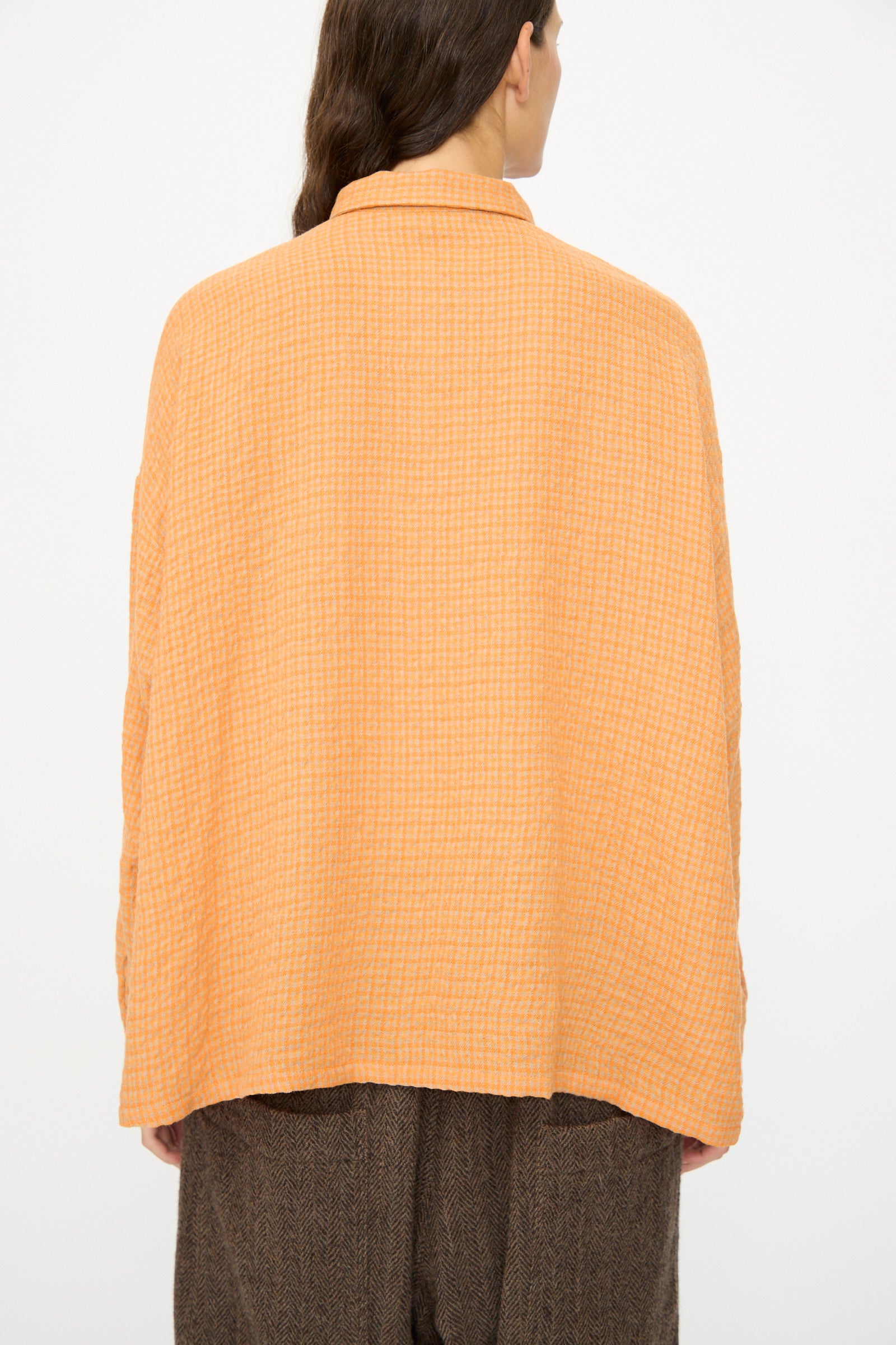 A person stands with their back to the camera, wearing the Ichi Antiquités Wool Cotton Gingham Shirt in Orange and Mocha, paired with brown pants, against a plain background.
