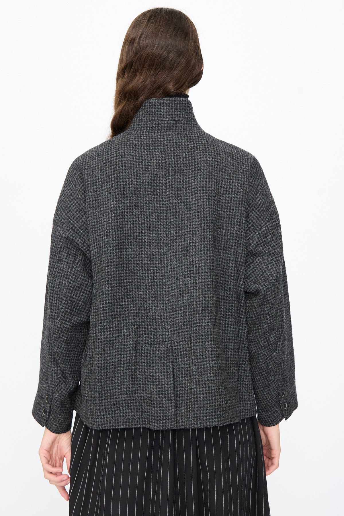 Back view of the Ichi Antiquités Wool Gauze Houndstooth Jacket in Charcoal, featuring a high neck and worn over a black pinstriped skirt.