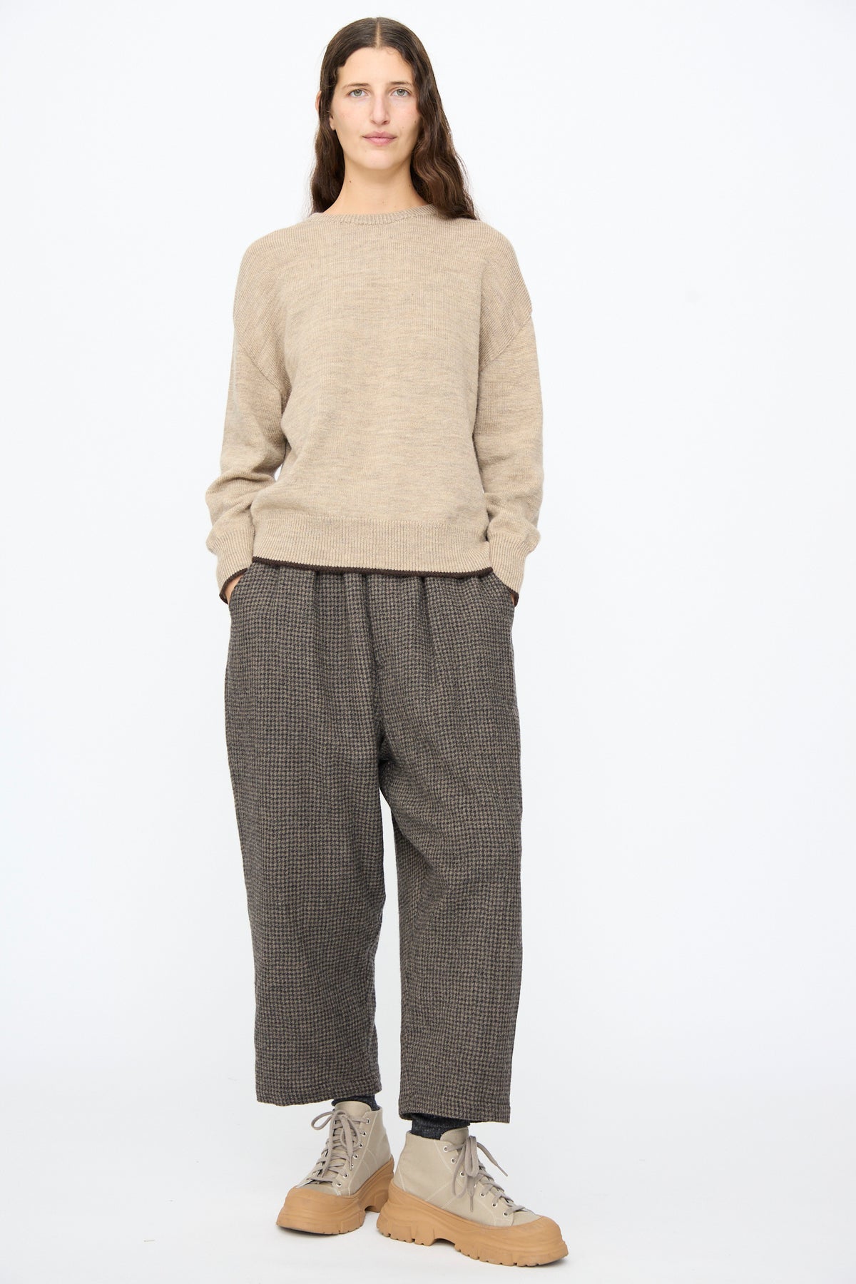 A person wearing a beige crewneck sweater, Ichi Antiquités Wool Gauze Houndstooth Pants in Mocha with an elastic waistband, and beige lace-up boots with chunky soles.