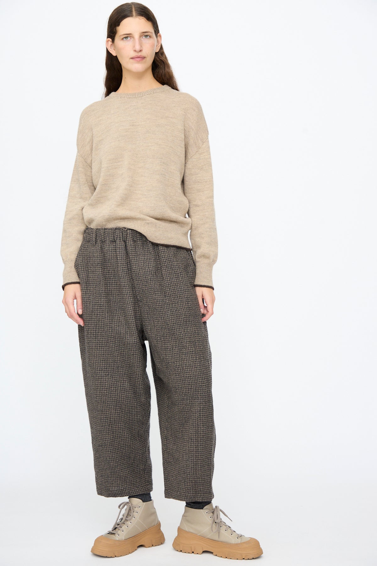A person wearing a beige sweater, relaxed fit Wool Gauze Houndstooth Pants in Mocha, and tan lace-up boots.