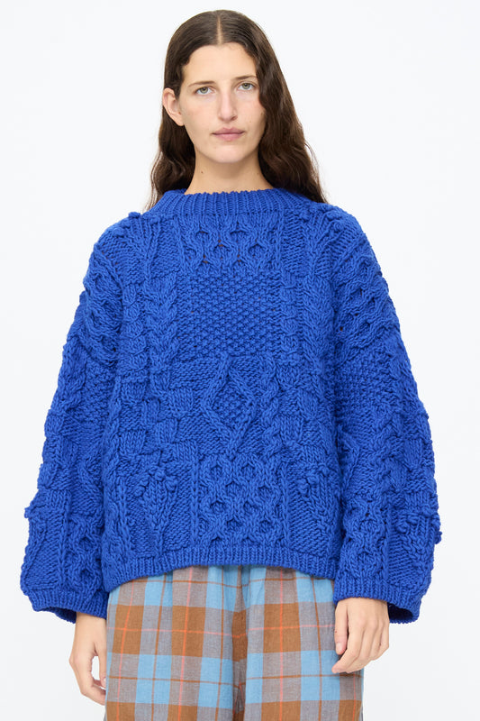 A person wearing an Ichi Antiquités Wool Hand Knit Pullover in Blue, an oversized cable knit sweater featuring chunky, textured diamond patterns.