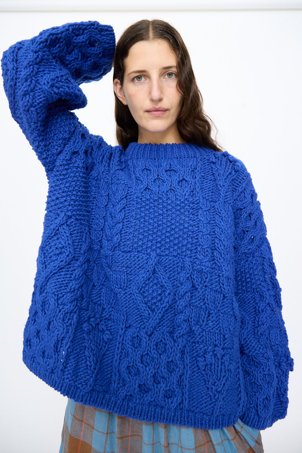 A person wears an Ichi Antiquités Wool Hand Knit Pullover in blue, featuring a chunky, oversized cable-knit design.